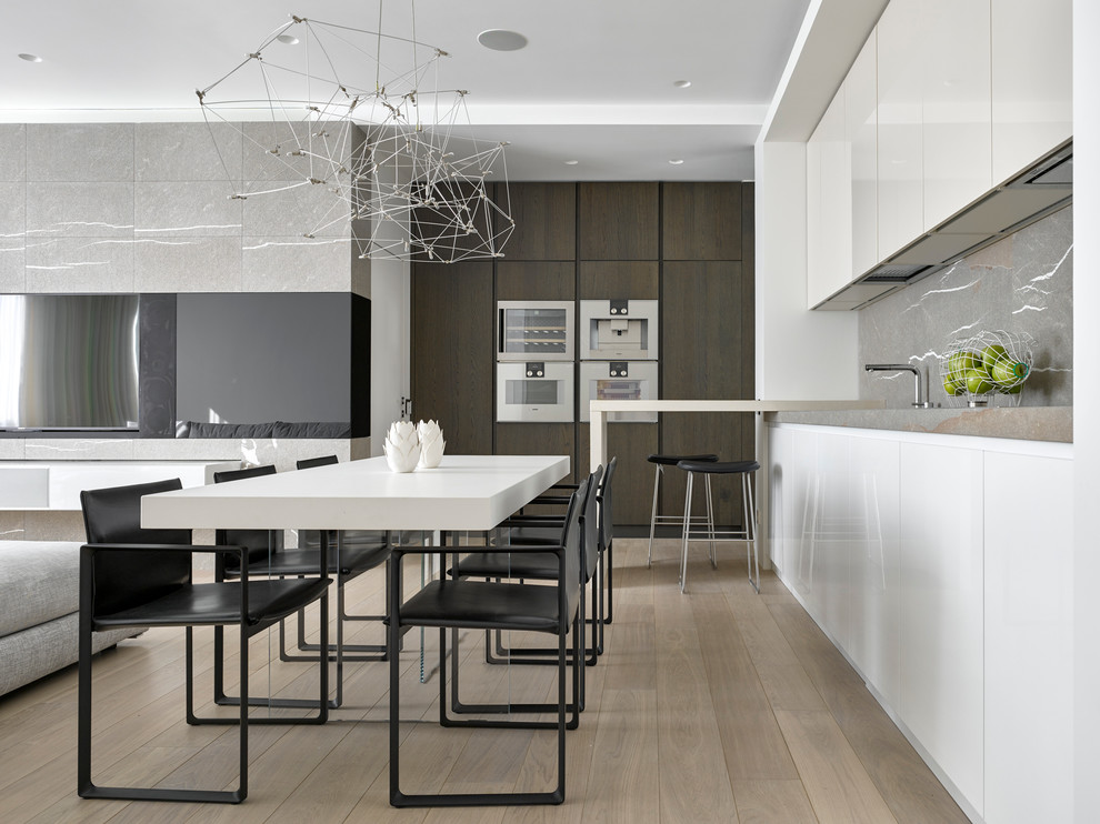 Photo of a contemporary l-shaped open plan kitchen in Moscow with flat-panel cabinets, white cabinets, grey splashback, stainless steel appliances, light hardwood flooring and a breakfast bar.