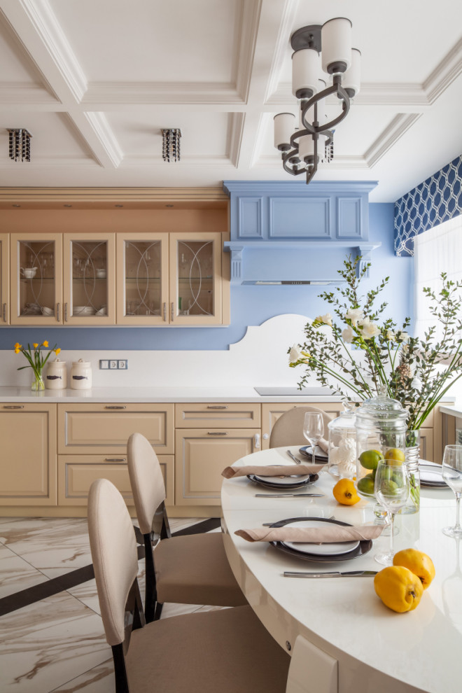 Стильный дизайн: светлая кухня в стиле неоклассика (современная классика) с обеденным столом, фасадами с выступающей филенкой, бежевыми фасадами, белым фартуком, бежевым полом и белой столешницей - последний тренд