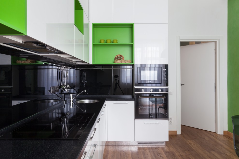 Modern inredning av ett avskilt, mellanstort l-kök, med släta luckor, vita skåp, svart stänkskydd, svarta vitvaror, en enkel diskho och brunt golv