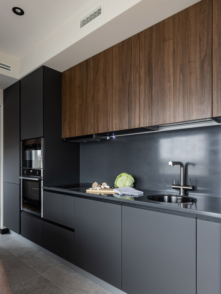 Свежая идея для дизайна: кухня в современном стиле с врезной мойкой, плоскими фасадами, черным фартуком, серым полом, серой столешницей и черными фасадами - отличное фото интерьера