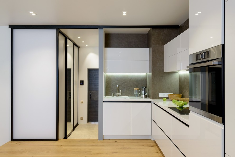 Photo of a contemporary l-shaped open plan kitchen in Moscow with a built-in sink, flat-panel cabinets, white cabinets, grey splashback, stainless steel appliances, medium hardwood flooring and no island.
