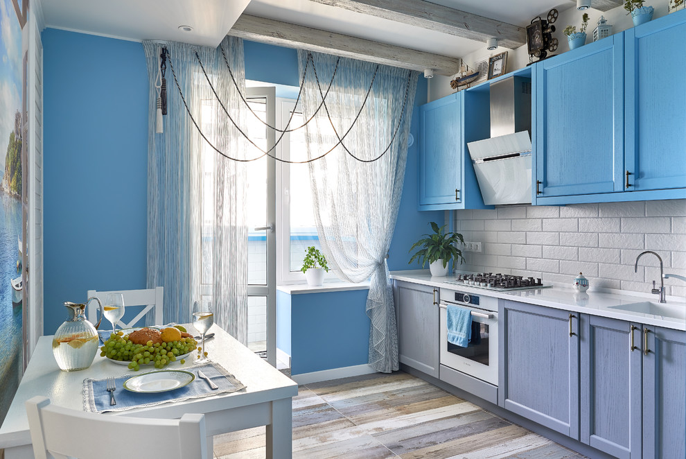 На фото: отдельная кухня в морском стиле с фасадами с утопленной филенкой, синими фасадами, белым фартуком, белой техникой, разноцветным полом и белой столешницей
