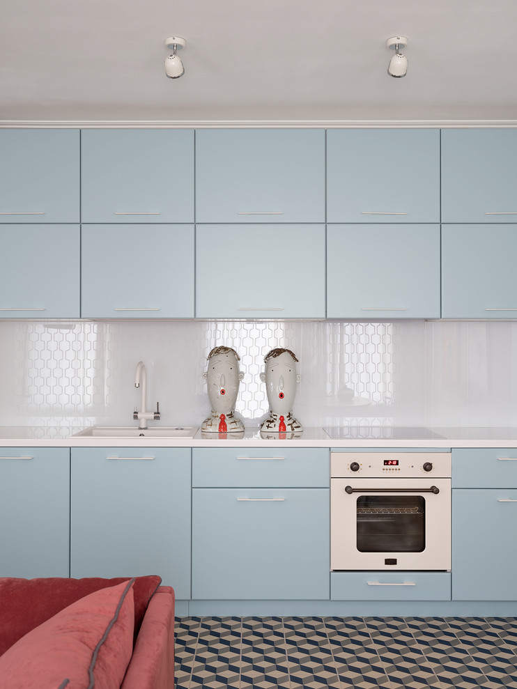 Cette image montre une cuisine linéaire vintage avec un évier posé, un placard à porte plane, des portes de placard bleues, une crédence blanche, un électroménager blanc et un plan de travail blanc.