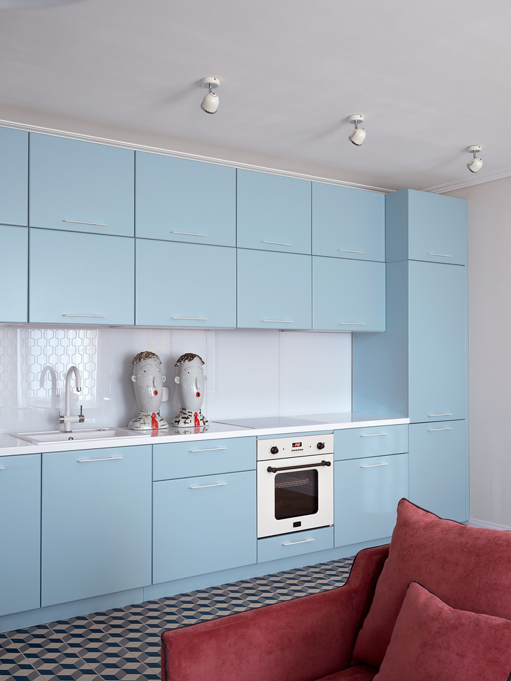 Cette image montre une cuisine linéaire vintage avec un évier posé, un placard à porte plane, des portes de placard bleues, une crédence blanche, un électroménager blanc et un plan de travail blanc.