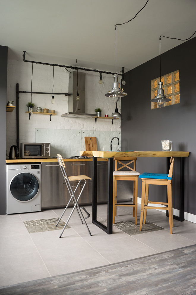 Foto på ett litet industriellt linjärt kök och matrum, med släta luckor, skåp i rostfritt stål, träbänkskiva och glaspanel som stänkskydd