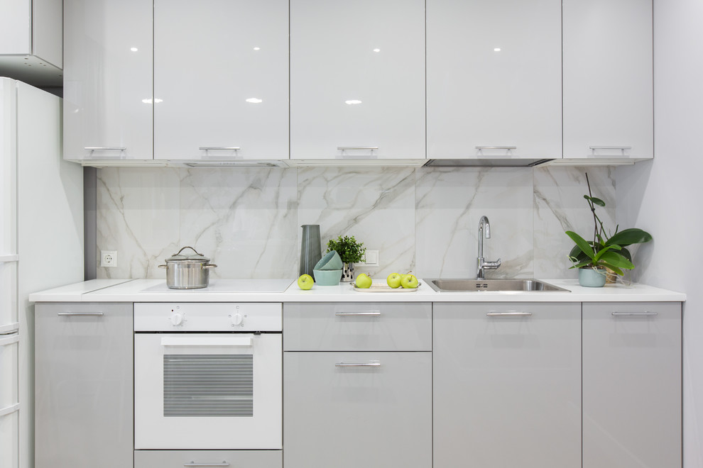 Idéer för att renovera ett litet vit linjärt vitt kök med öppen planlösning, med en nedsänkt diskho, släta luckor, grå skåp, laminatbänkskiva, grått stänkskydd, stänkskydd i porslinskakel, vita vitvaror, laminatgolv och beiget golv