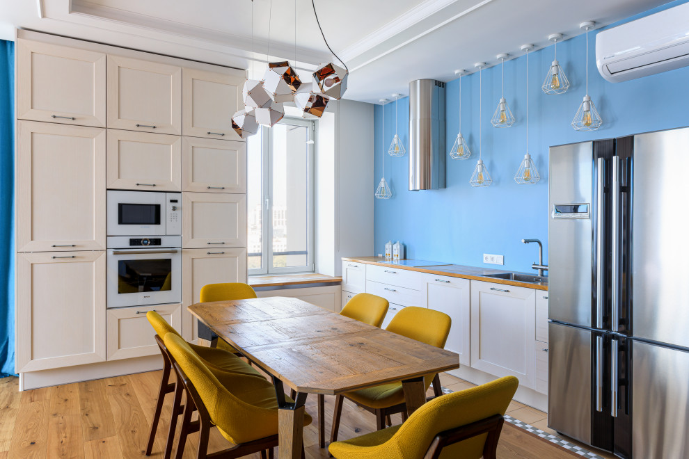 This is an example of a large scandi galley kitchen/diner in Moscow with a built-in sink, recessed-panel cabinets, white cabinets, wood worktops, blue splashback, white appliances, medium hardwood flooring, no island, brown floors and beige worktops.