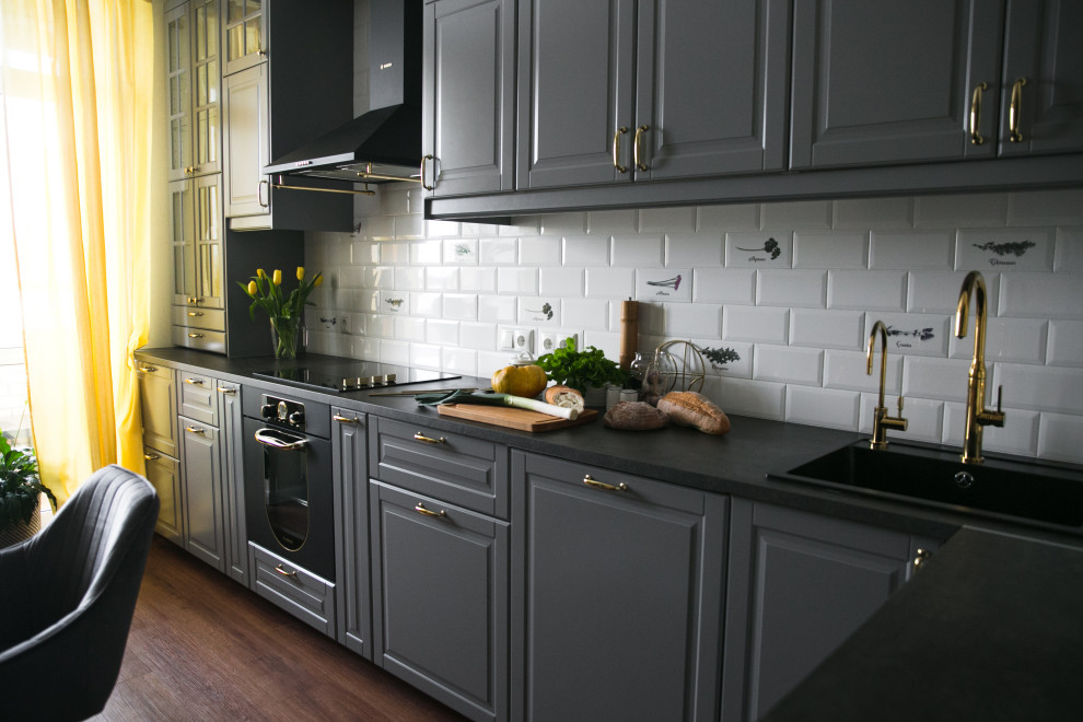 Inredning av ett nordiskt mellanstort svart svart kök, med en nedsänkt diskho, luckor med upphöjd panel, grå skåp, bänkskiva i koppar, vitt stänkskydd, stänkskydd i keramik, svarta vitvaror, vinylgolv och brunt golv