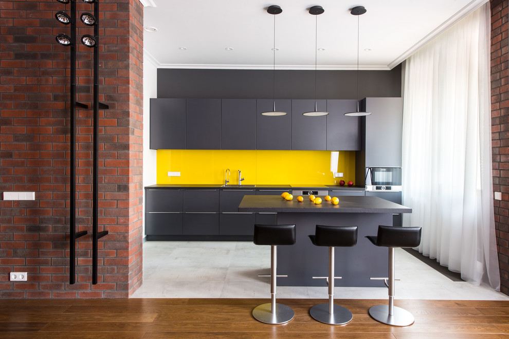 Trendy single-wall white floor open concept kitchen photo in Moscow with flat-panel cabinets, black cabinets, yellow backsplash, glass sheet backsplash, an island, black countertops and stainless steel appliances