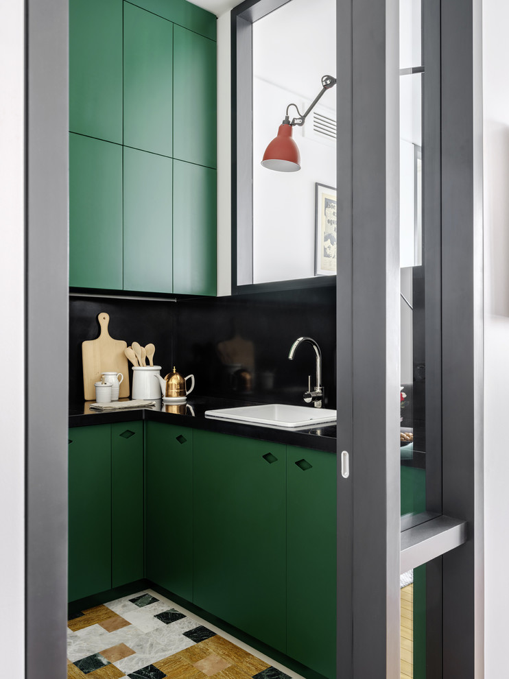 Foto på ett avskilt, litet funkis svart kök, med en nedsänkt diskho, släta luckor, gröna skåp, svart stänkskydd och flerfärgat golv