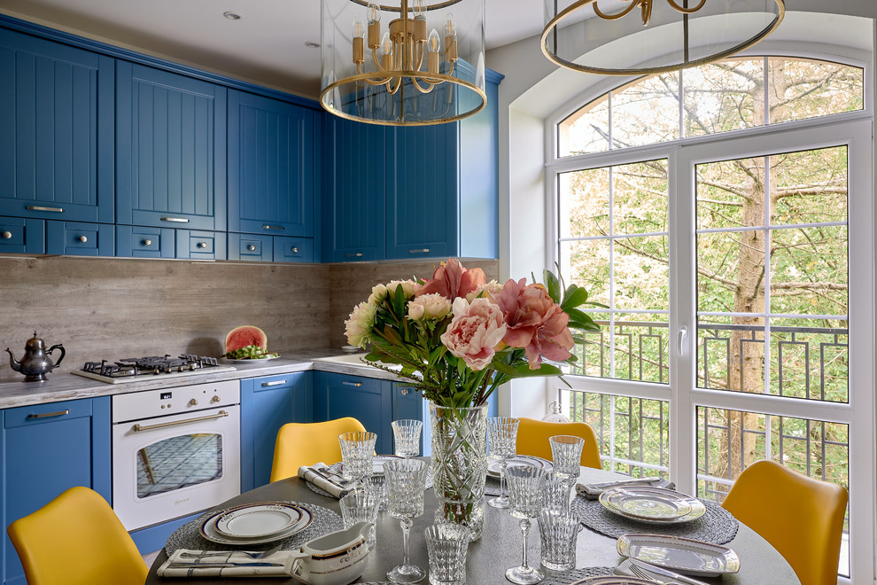 Источник вдохновения для домашнего уюта: угловая кухня в стиле неоклассика (современная классика) с обеденным столом, фасадами в стиле шейкер, синими фасадами, бежевым фартуком, белой техникой и разноцветным полом без острова