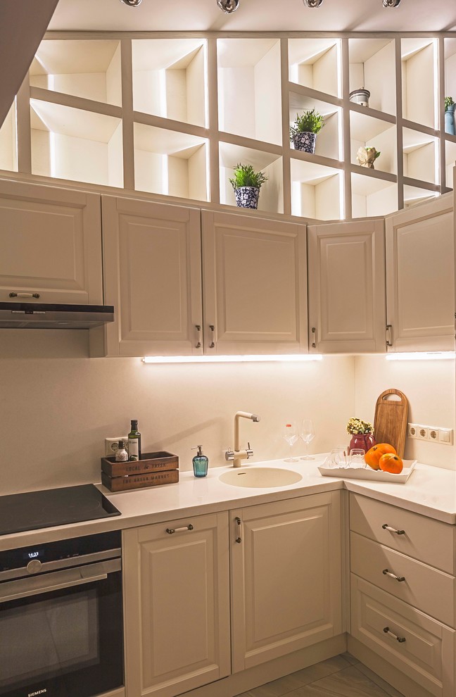 На фото: угловая кухня в современном стиле с монолитной мойкой, белыми фасадами, белым фартуком и фасадами с выступающей филенкой без острова