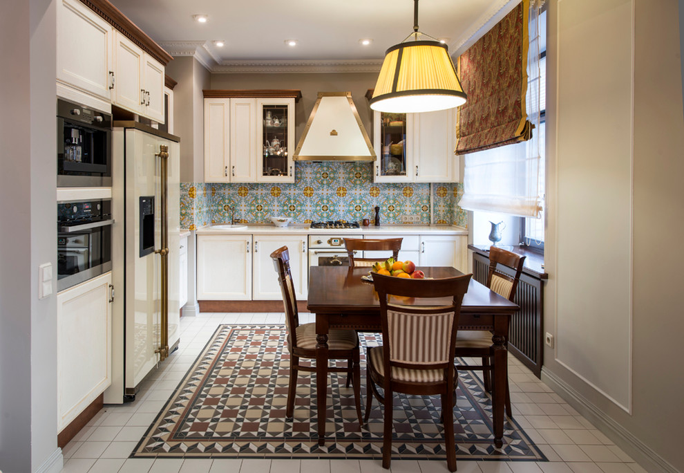 Стильный дизайн: угловая кухня-гостиная в классическом стиле с фасадами с утопленной филенкой, белыми фасадами, синим фартуком и шторами на окнах без острова - последний тренд