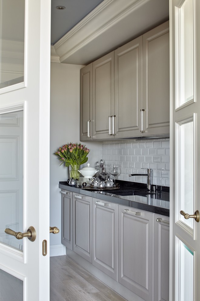 Cette image montre une cuisine linéaire design avec un placard avec porte à panneau surélevé, des portes de placard grises, une crédence blanche et parquet clair.