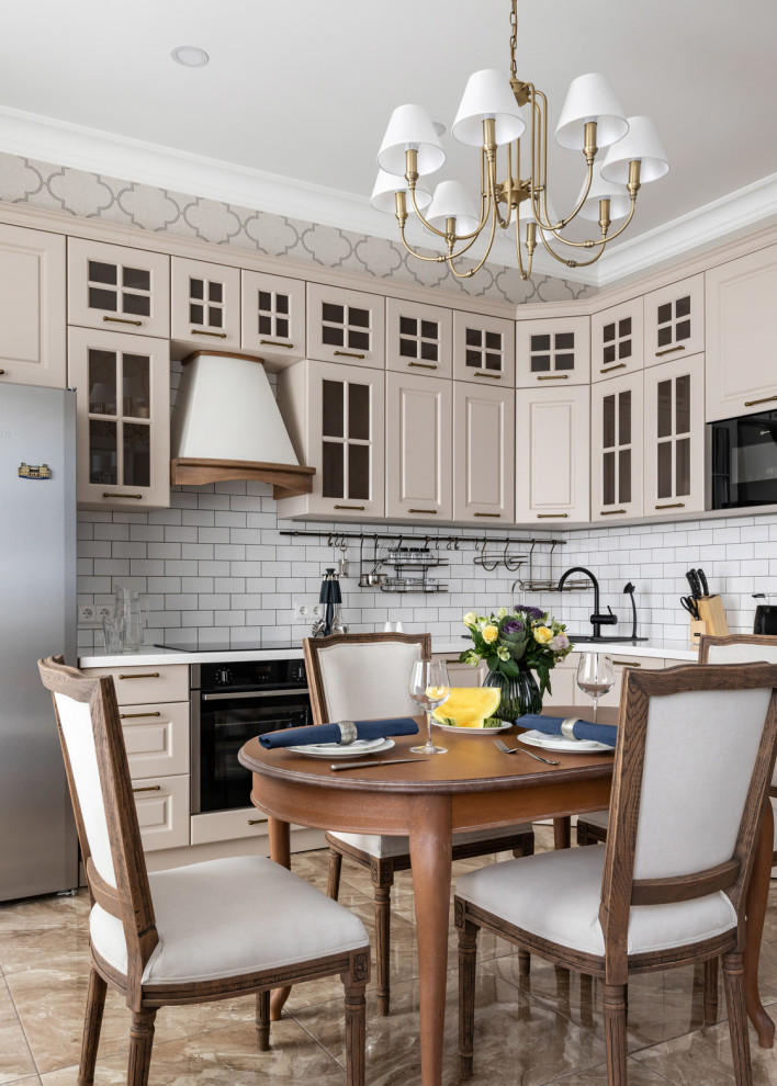 Traditional l-shaped kitchen in Saint Petersburg with glass-front cabinets, beige cabinets, white splashback, metro tiled splashback, black appliances, beige floors and white worktops.