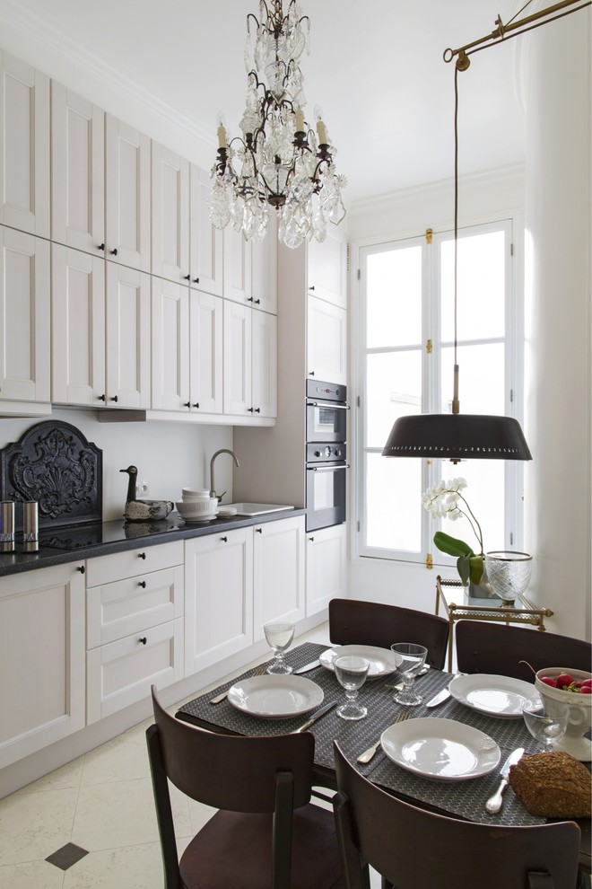 Klassisk inredning av ett svart linjärt svart kök och matrum, med luckor med infälld panel, vita skåp, en nedsänkt diskho, vitt stänkskydd, svarta vitvaror och beiget golv