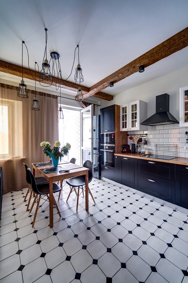 Imagen de cocina de estilo de casa de campo cerrada sin isla con armarios estilo shaker, puertas de armario negras, encimera de madera, salpicadero blanco, salpicadero de azulejos tipo metro, electrodomésticos negros y suelo blanco