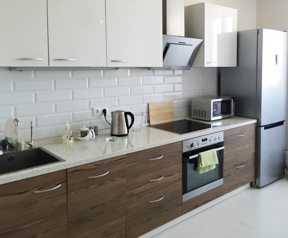 Example of a mid-sized danish single-wall ceramic tile and white floor eat-in kitchen design in Saint Petersburg with an undermount sink, flat-panel cabinets, medium tone wood cabinets, solid surface countertops, white backsplash, subway tile backsplash, stainless steel appliances, no island and beige countertops