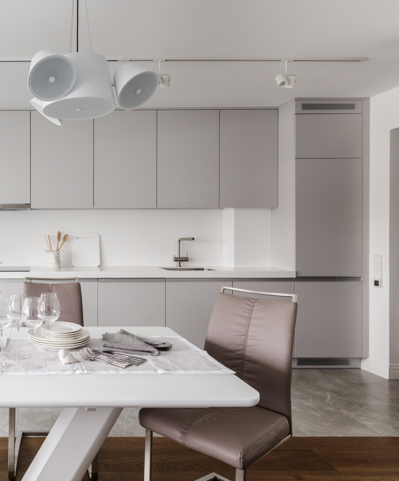 Foto på ett funkis vit linjärt kök och matrum, med släta luckor, grå skåp, integrerade vitvaror och grått golv
