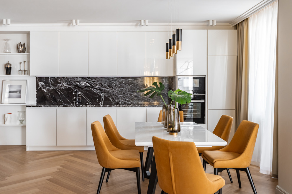 Medium sized contemporary single-wall kitchen in Other with flat-panel cabinets, white cabinets, black splashback, black appliances, light hardwood flooring, beige floors and black worktops.