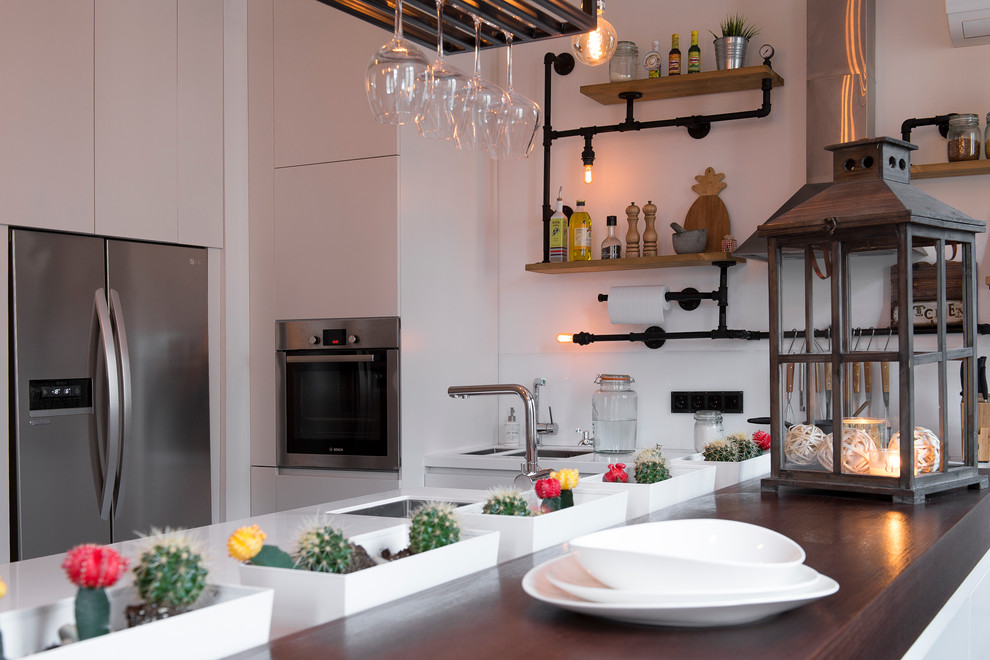 Exempel på ett mellanstort industriellt linjärt kök med öppen planlösning, med en undermonterad diskho, släta luckor, vita skåp, bänkskiva i koppar, vitt stänkskydd, glaspanel som stänkskydd, rostfria vitvaror, laminatgolv, en köksö och brunt golv