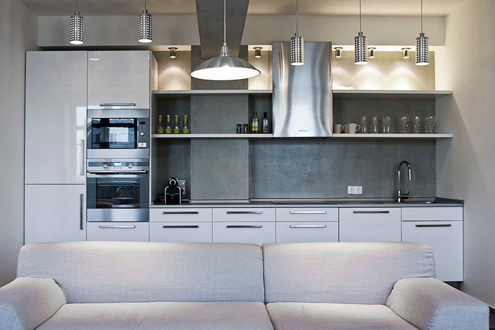 Immagine di una cucina industriale con ante lisce, ante bianche, paraspruzzi grigio, elettrodomestici in acciaio inossidabile e nessuna isola