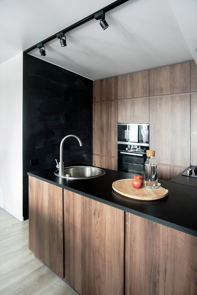 Exemple d'une cuisine tendance en bois brun et U avec un évier posé, un placard à porte plane, un électroménager noir, une péninsule, plan de travail noir et un sol beige.