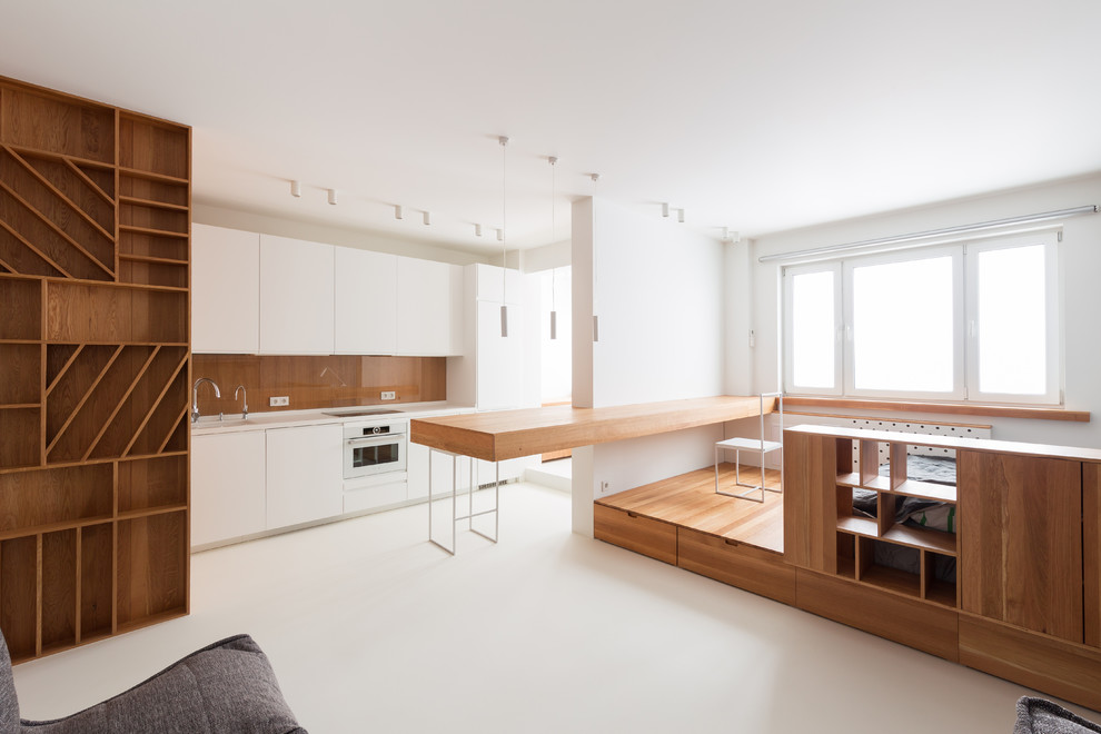На фото: параллельная кухня в стиле модернизм с белым полом, плоскими фасадами, белыми фасадами, белой техникой, полуостровом и белой столешницей