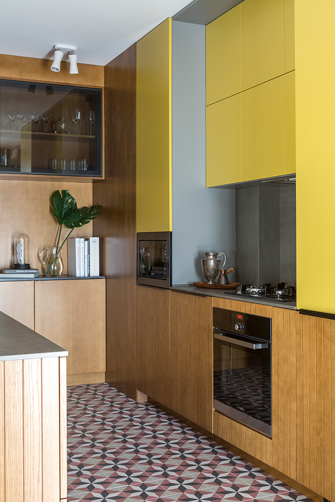 Imagen de cocina bohemia cerrada sin isla con armarios con paneles lisos, puertas de armario amarillas, salpicadero verde, electrodomésticos de acero inoxidable y suelo multicolor