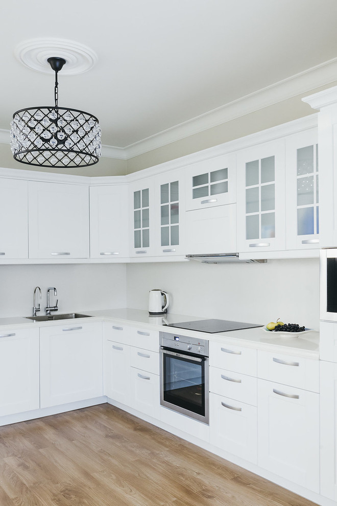 На фото: угловая кухня в современном стиле с врезной мойкой, белыми фасадами, белым фартуком, коричневым полом и белой столешницей