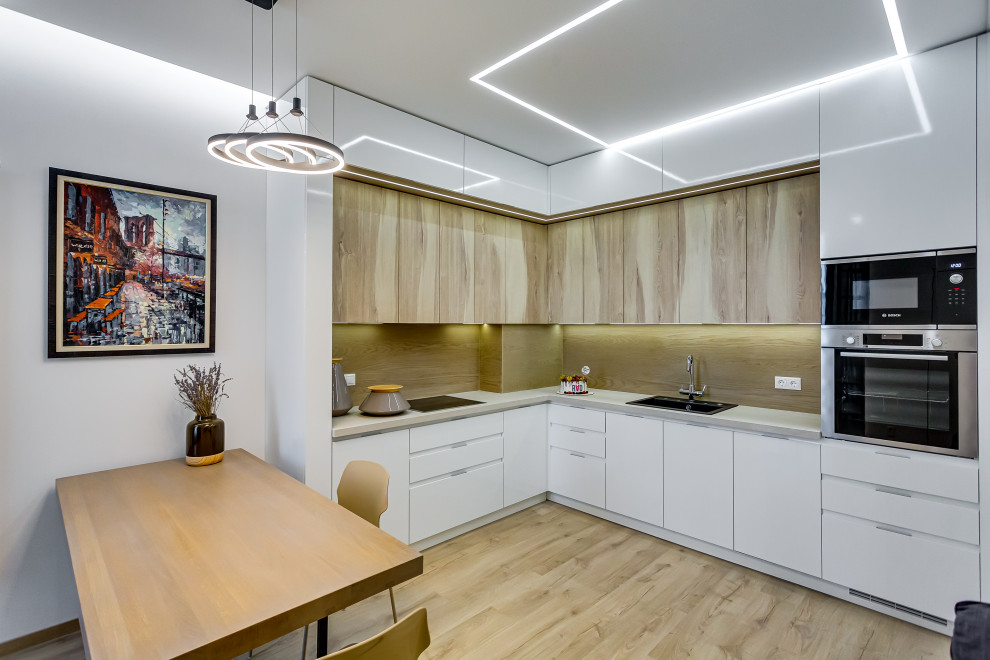 Medium sized contemporary l-shaped kitchen/diner in Other with a built-in sink, flat-panel cabinets, white cabinets, beige splashback, stainless steel appliances, no island, beige floors and grey worktops.