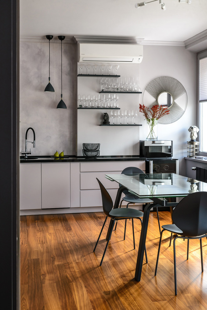 Photo of a contemporary enclosed kitchen in Novosibirsk with flat-panel cabinets, grey cabinets, grey splashback, medium hardwood flooring, brown floors and black worktops.