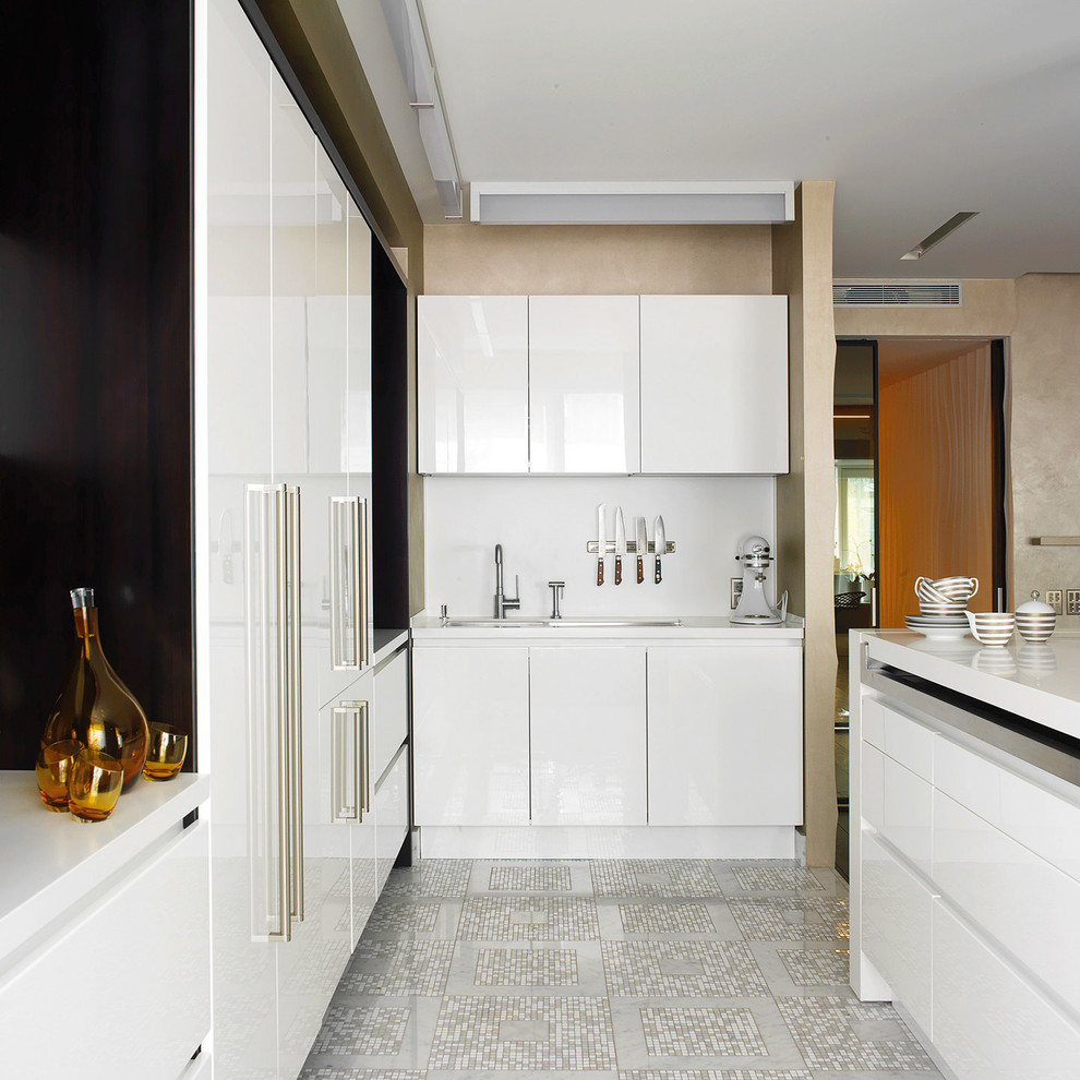 Modern inredning av ett kök, med en undermonterad diskho, släta luckor, vita skåp, vitt stänkskydd, marmorgolv, en köksö och grått golv