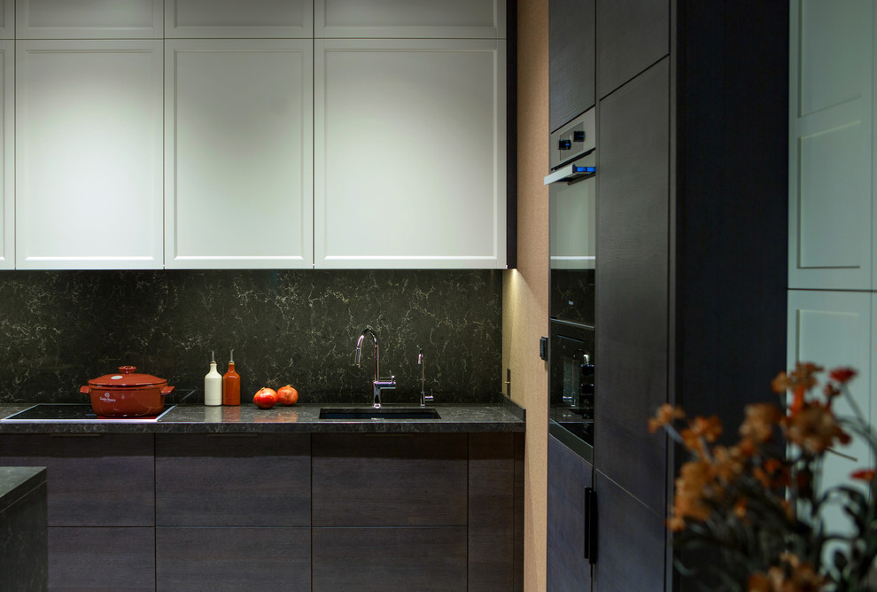 Foto di un cucina con isola centrale design con ante con riquadro incassato, ante beige, paraspruzzi nero, elettrodomestici neri e top nero