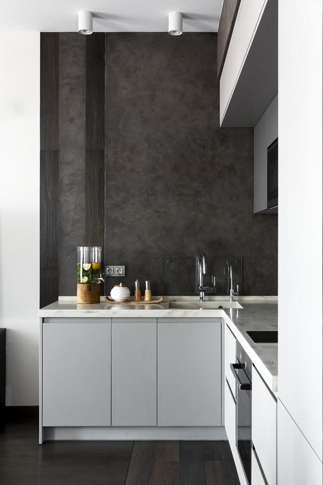 Design ideas for a small contemporary l-shaped open plan kitchen in Moscow with an integrated sink, flat-panel cabinets, grey cabinets, composite countertops, grey splashback, black appliances, porcelain flooring, no island, brown floors and beige worktops.