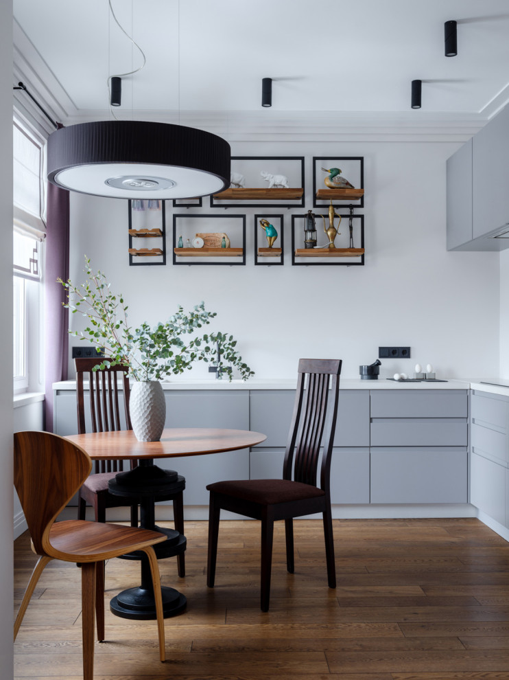 This is an example of a medium sized contemporary l-shaped kitchen/diner in Moscow with flat-panel cabinets, grey cabinets, integrated appliances, medium hardwood flooring, no island, brown floors and white worktops.