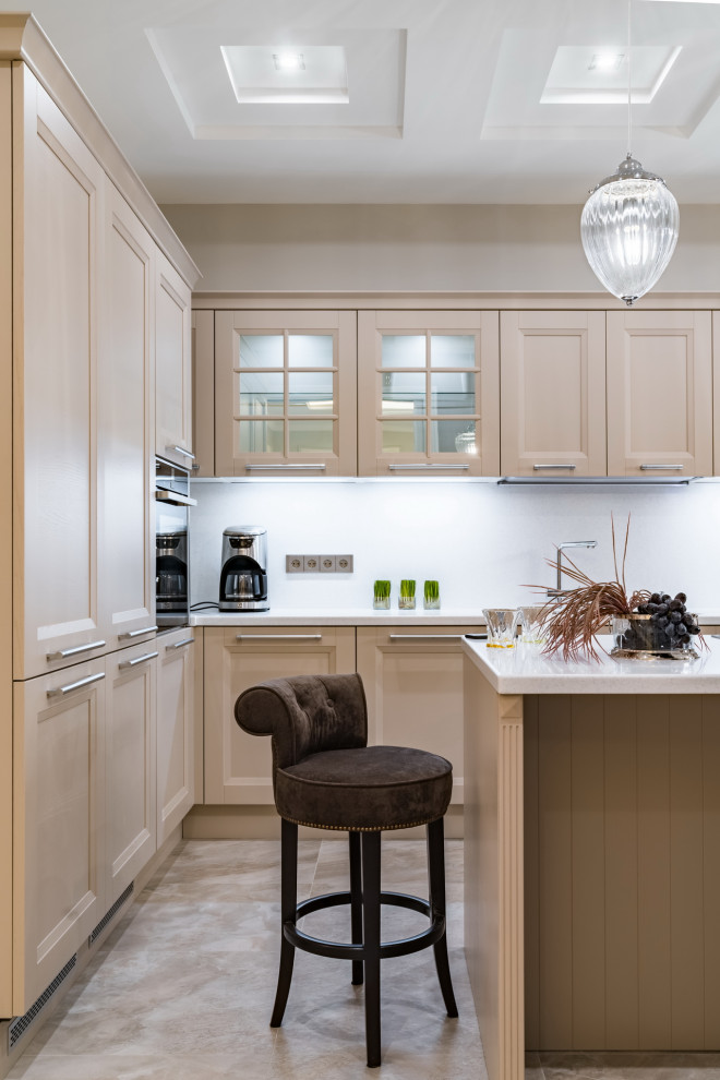 На фото: угловая, светлая кухня среднего размера в современном стиле с фасадами с утопленной филенкой, бежевыми фасадами, техникой под мебельный фасад, островом, серым полом и белой столешницей
