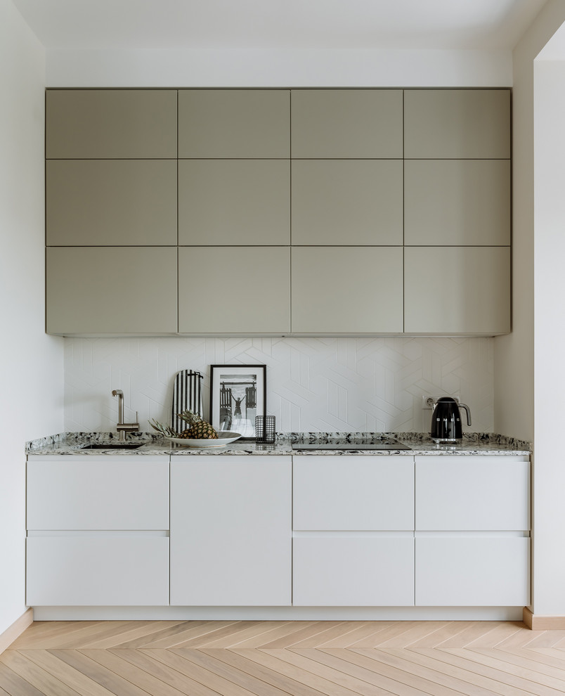 Cette image montre une petite cuisine linéaire et bicolore design avec un placard à porte plane, une crédence blanche, parquet clair et un sol beige.