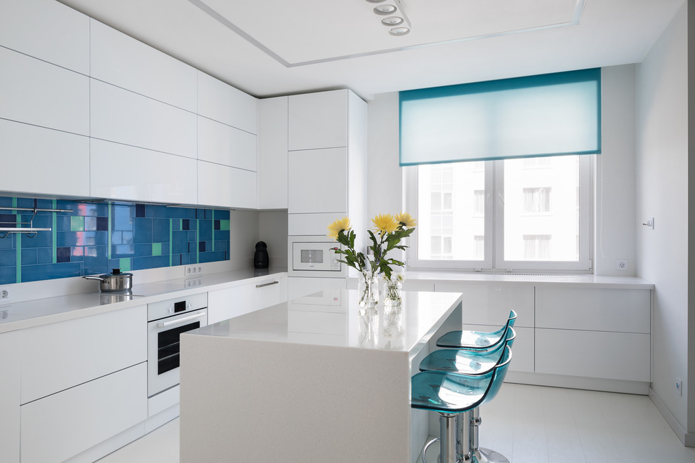 Пример оригинального дизайна: угловая, светлая кухня в современном стиле с плоскими фасадами, белыми фасадами, синим фартуком, белой техникой, островом, белым полом и белой столешницей