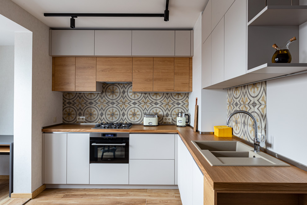 Medium sized contemporary kitchen/diner in Saint Petersburg with a built-in sink, flat-panel cabinets, white cabinets, wood worktops, multi-coloured splashback, ceramic splashback, black appliances, laminate floors, no island, brown floors, brown worktops and a drop ceiling.
