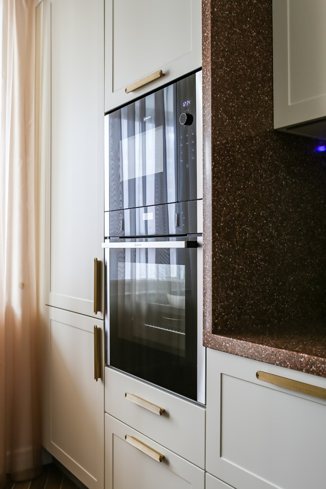 Klassische Wohnküche mit flächenbündigen Schrankfronten, Mineralwerkstoff-Arbeitsplatte, Küchenrückwand in Braun, schwarzen Elektrogeräten und brauner Arbeitsplatte in Sankt Petersburg