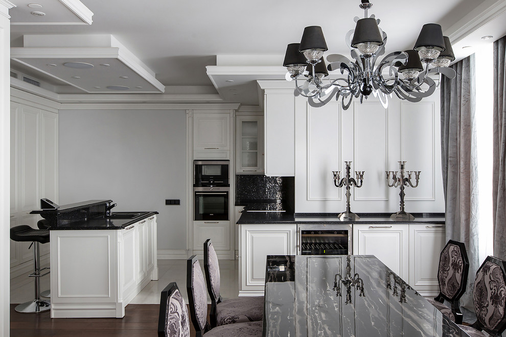 Стильный дизайн: кухня-гостиная в стиле неоклассика (современная классика) с белыми фасадами, черным фартуком, фартуком из плитки мозаики, техникой из нержавеющей стали и островом - последний тренд