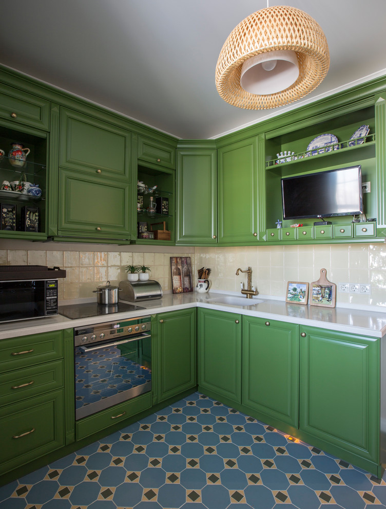На фото: отдельная, угловая кухня в современном стиле с одинарной мойкой, фасадами с выступающей филенкой, зелеными фасадами, бежевым фартуком, техникой из нержавеющей стали, синим полом и белой столешницей с