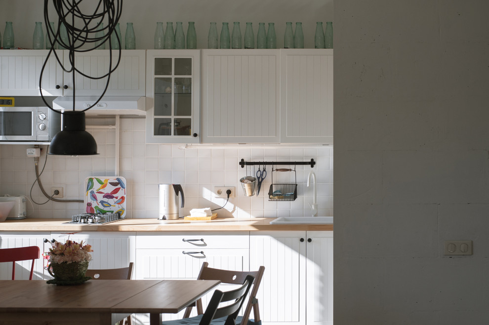 Bild på ett mellanstort skandinaviskt linjärt kök med öppen planlösning, med vita skåp, träbänkskiva, vitt stänkskydd, stänkskydd i keramik och en nedsänkt diskho
