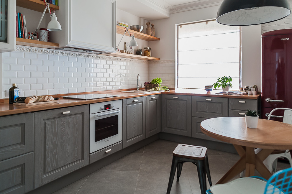 Small scandi grey and white l-shaped kitchen/diner in Other with a built-in sink, grey cabinets, wood worktops, grey floors, brown worktops, raised-panel cabinets, white splashback, ceramic splashback, white appliances and porcelain flooring.