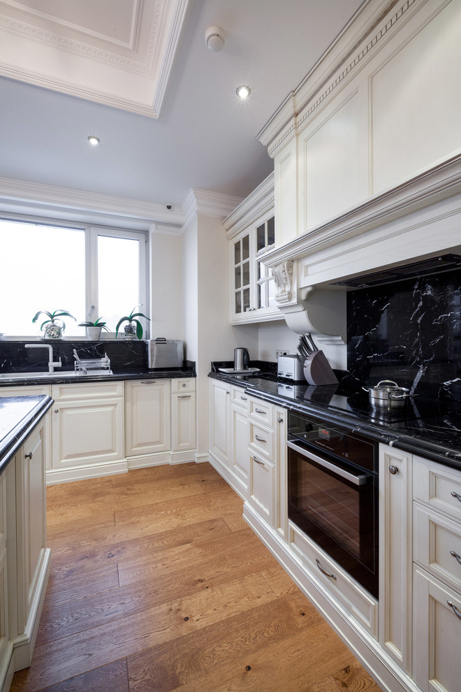 Photo of a large traditional u-shaped kitchen/diner in Moscow with a built-in sink, raised-panel cabinets, white cabinets, marble worktops, white splashback, marble splashback, black appliances, painted wood flooring and an island.