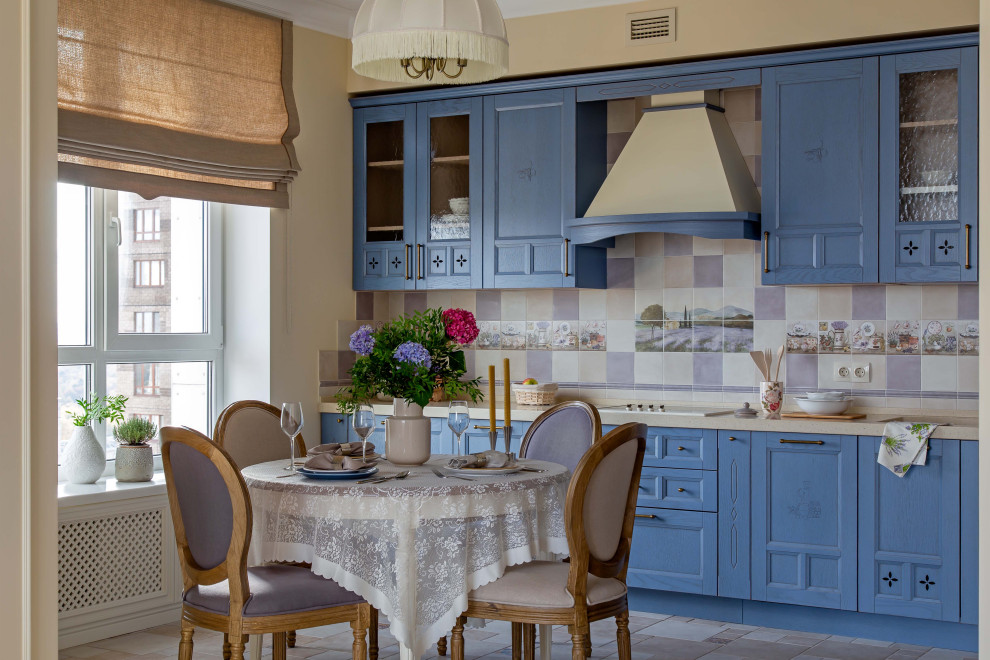 Стильный дизайн: прямая кухня в классическом стиле с обеденным столом, фасадами с утопленной филенкой, синими фасадами, разноцветным фартуком, бежевым полом и бежевой столешницей без острова - последний тренд