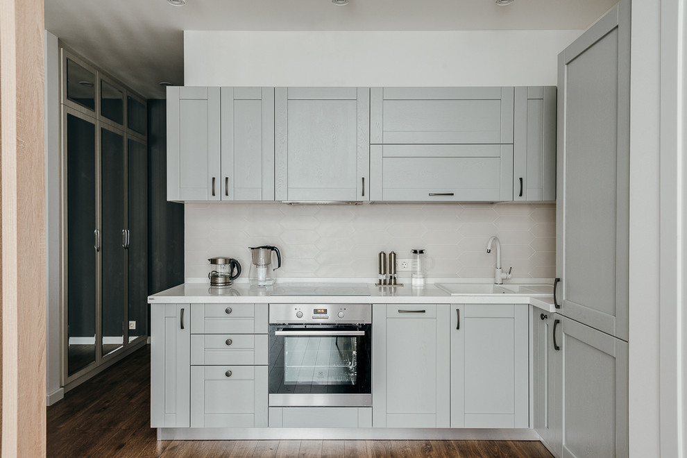 Diseño de cocinas en L escandinava con fregadero encastrado, armarios estilo shaker, puertas de armario grises, salpicadero blanco, electrodomésticos de acero inoxidable y encimeras blancas