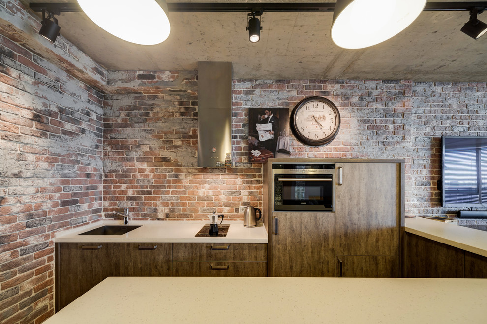 Industriell inredning av ett kök, med släta luckor, bruna skåp, rött stänkskydd, svarta vitvaror, en halv köksö och en enkel diskho