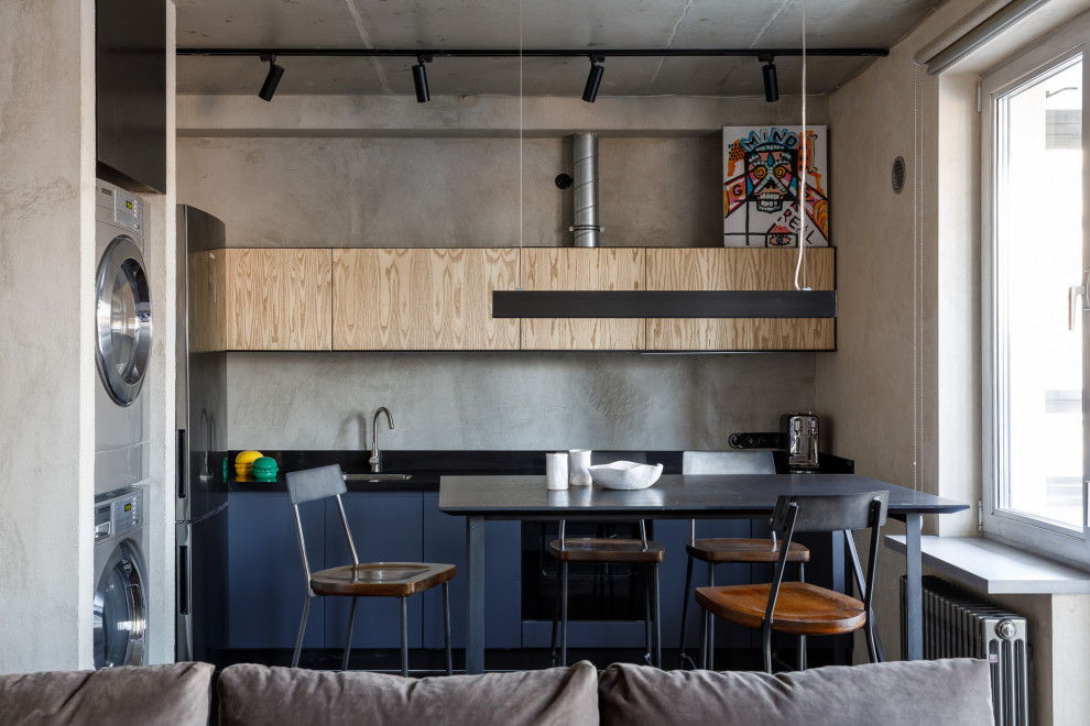 Exemple d'une cuisine ouverte linéaire et bicolore industrielle avec des portes de placard bleues, une crédence grise, aucun îlot et plan de travail noir.